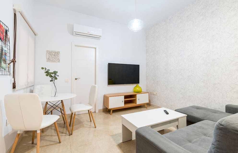General view of the living-dining room, with air conditioning, TV, tables and chairs, and a chaise longue sofa.