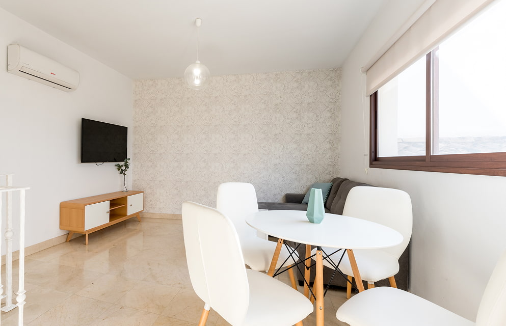 Living room in one of Hoteles del Sur’s apartments, with a TV, air conditioning, a sofa and a table and chair set