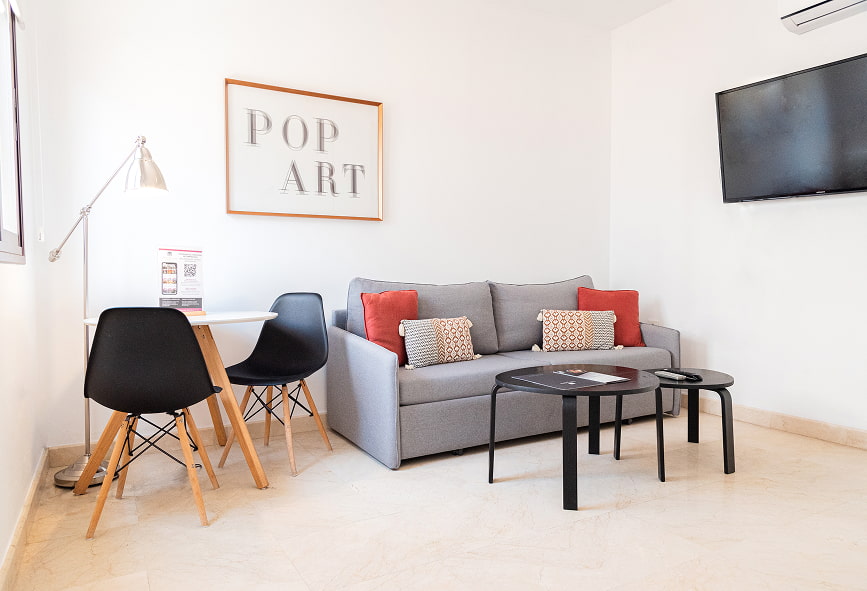 Duplex com Varanda | Sala Área com sofá, TV, mesa com duas cadeiras e um quadro de Pop Art