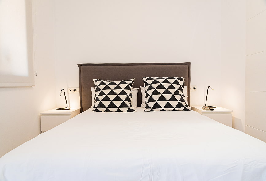 Duplex com varanda | Detalhe da cama Detalhe da cama do quarto, com lençóis brancos e almofadas com triângulos brancos e pretos