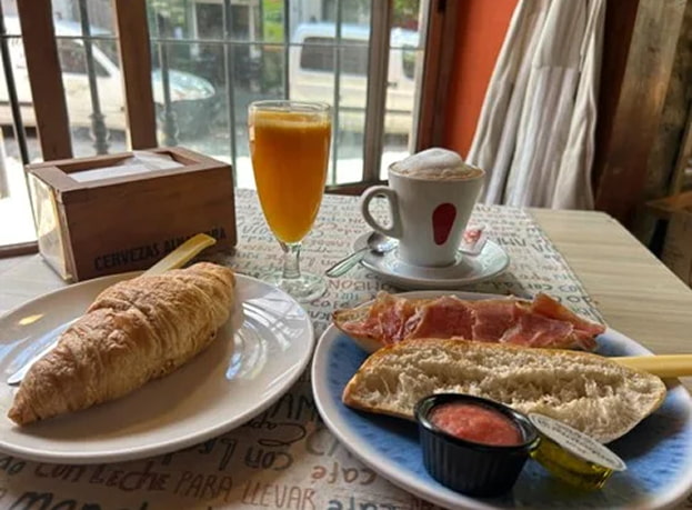 Desayuno Desayuno compuesto por zumo de naranja, café, croissant y tostadas de jamón serrano con tomate